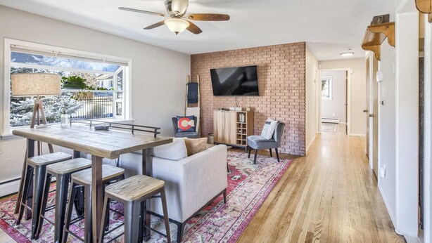 A modern living room with a dining area, a brick accent wall, a flat-screen TV, and a ceiling fan. - 5BR 💖heart Of Old Colorado Cityfoosball 💖 (Colorado Springs)