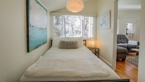 A bedroom with a bed, a window, a hanging light fixture, and a painting on the wall. - 1bdcute Tiny Housenear Olympic Training Center (Colorado Springs)