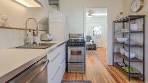 A compact kitchen with a gas stove, oven, and a built-in sink. There is a small dining area with a table and chairs, and a shelf with dishes. - 1bdcute Tiny Housenear Olympic Training Center (Colorado Springs)
