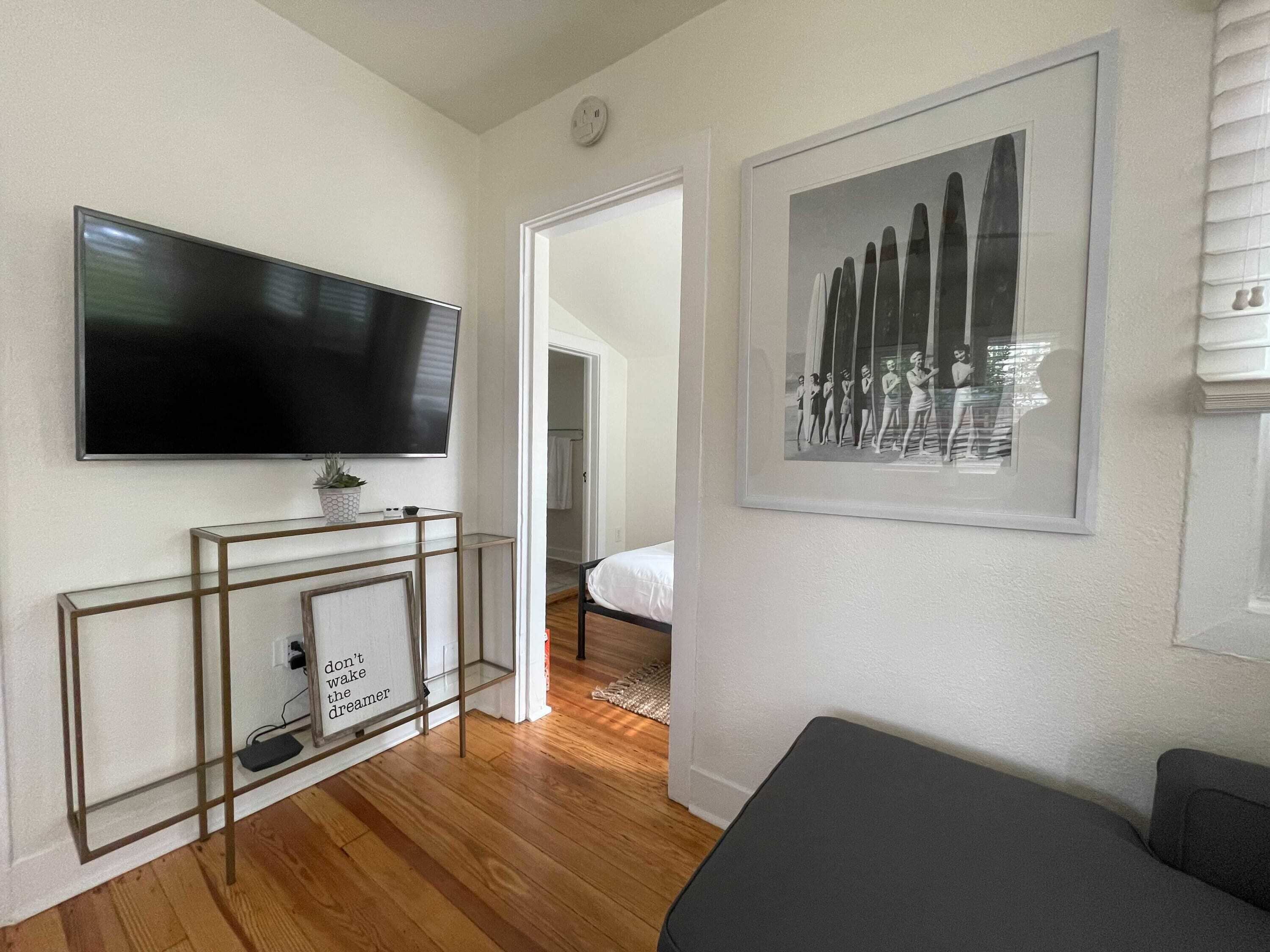 A modern bedroom with a flat-screen TV, a framed picture, and a bedside table.