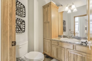 A bathroom with a toilet, wooden cabinets, a marble countertop, a sink, and a mirror.
