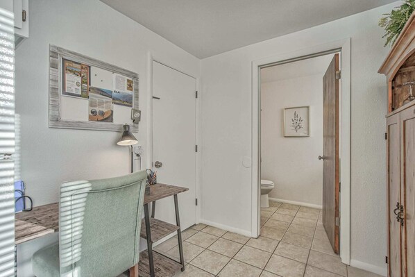 Une petite salle de bain comprenant des toilettes, un petit lavabo et un espace douche. Une porte donne accès à une autre pièce, et un tableau encadré est accroché au mur.