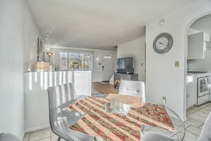 A modern living room with a glass dining table, two chairs, a television, and a kitchen area with a stove and oven. - 2bdcentrally Locatedclose to Shops & Restaurants! (Colorado Springs)