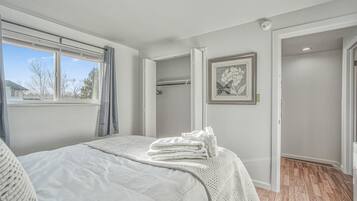 A bedroom with a bed, a window, a door, and a framed picture on the wall.