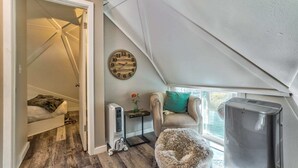 A cozy attic bedroom with a sloped ceiling, a wooden clock, a pet bed, a heater, and a refrigerator.