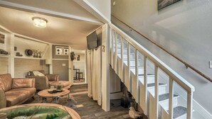 A spacious living room with a leather sofa, a coffee table, and a glass-top table with decorative items. A staircase with a wooden handrail leads to an upper level.