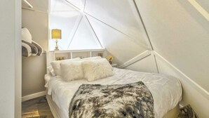 A bedroom with a bed, pillows, a lamp, and a window.