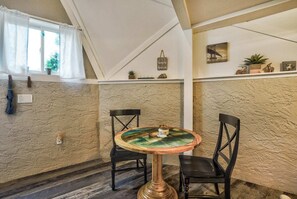 A cozy room with a round table, two chairs, a window with curtains, a textured wall, a shelf with decorative items, and a small plant. - Crystal Cabin Pikes Peak Mountain w/ Wine Cellar (Divide)