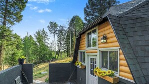 A cabin with a wooden exterior, a deck with a bench, and a window with sunflowers.