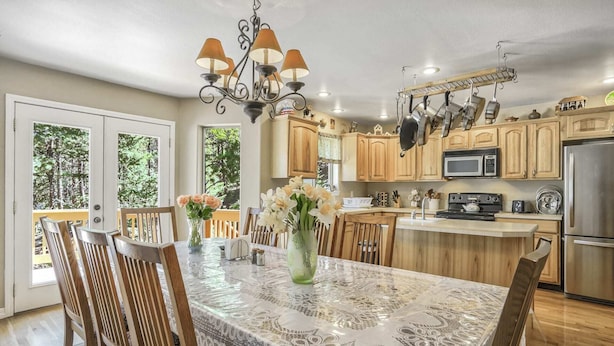 A kitchen with wooden cabinets, a stainless steel refrigerator, and a dining area with a table covered by a lace tablecloth. - 6bdfamily Mountain Getawayhot Tubminutes to Pikes Peak and Charis College (Woodland Park)