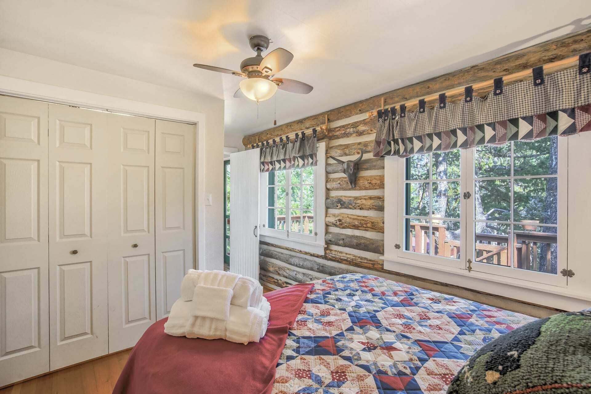 Quarto de cabana de tronco com uma cama, um ventilador de teto e uma janela com vista para o exterior.
