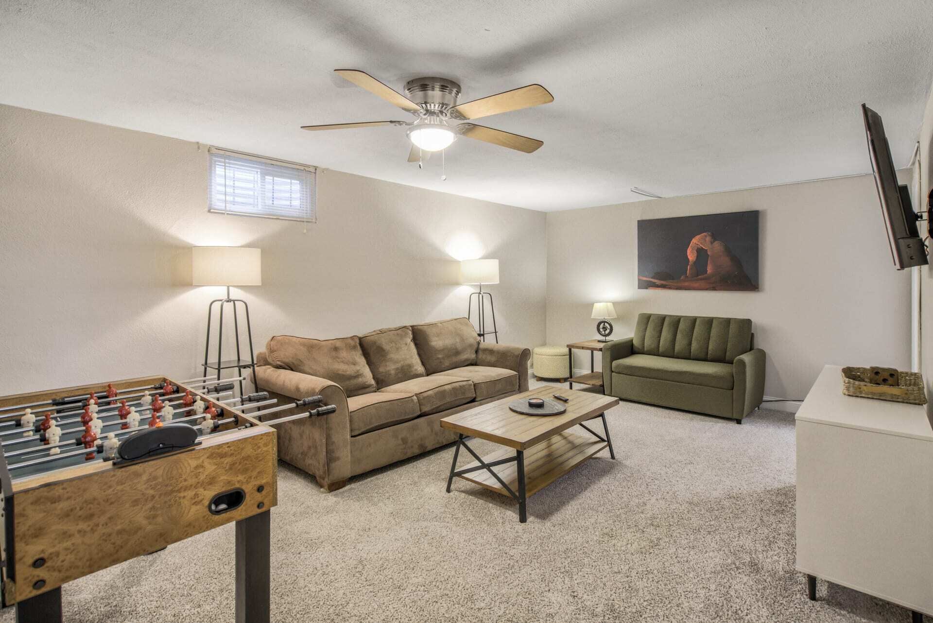 Ein Wohnzimmer mit Sofa, Couchtisch, Kicker, Deckenventilator und einem Gemälde an der Wand.