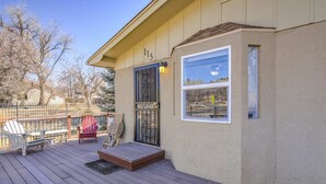 Una terraza techada con sillas Adirondack, una mesita y una puerta con ventana.