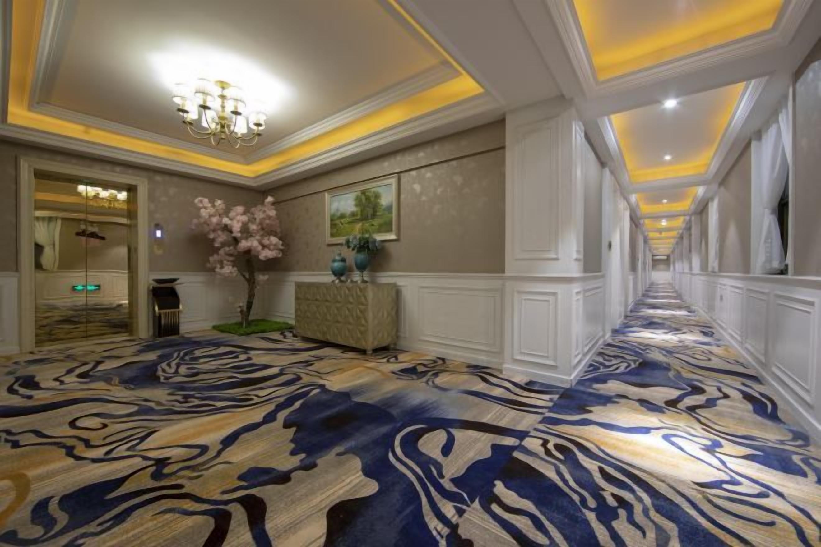 A hotel hallway with a patterned carpet, a chandelier, a reception desk, and a framed picture on the wall.