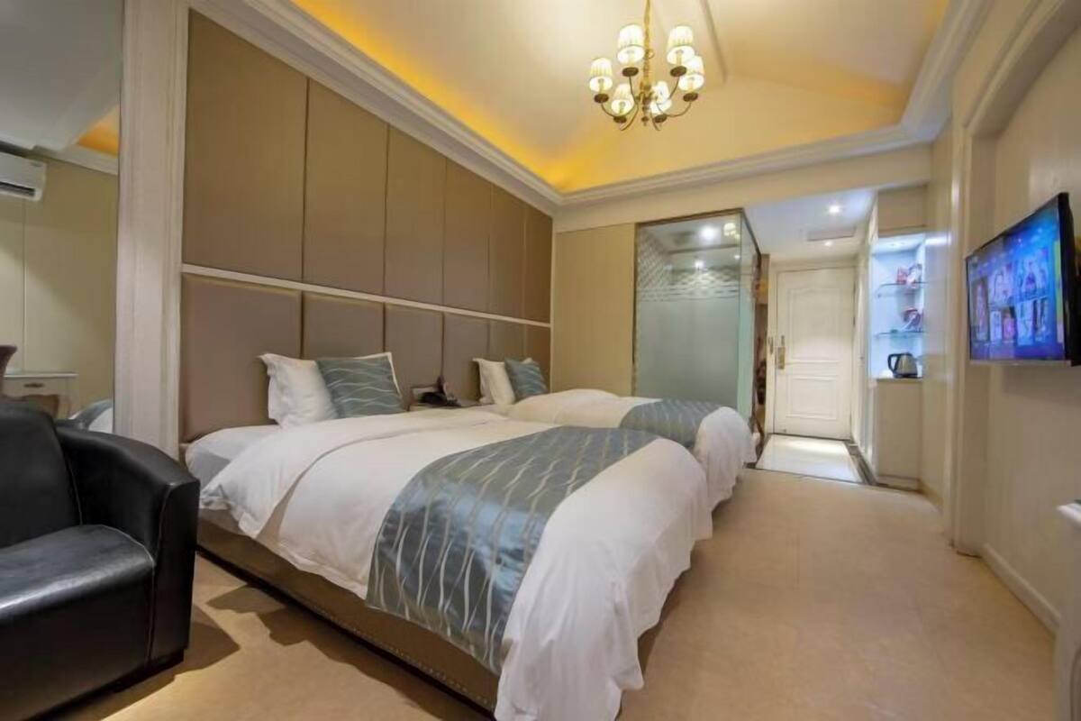 Quarto de hotel com uma cama grande, uma televisão na parede e um candelabro.