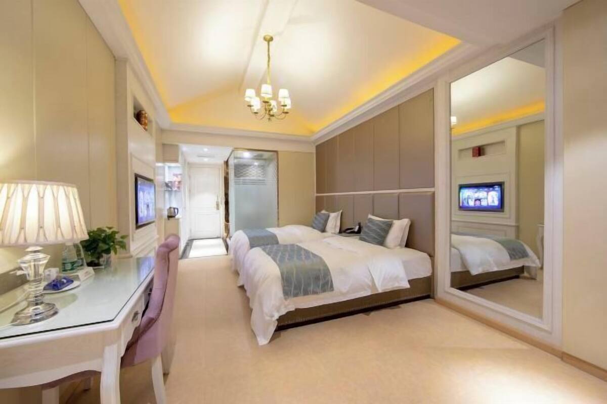 Quarto de hotel com cama, escrivaninha com luminária, televisão e espelho.