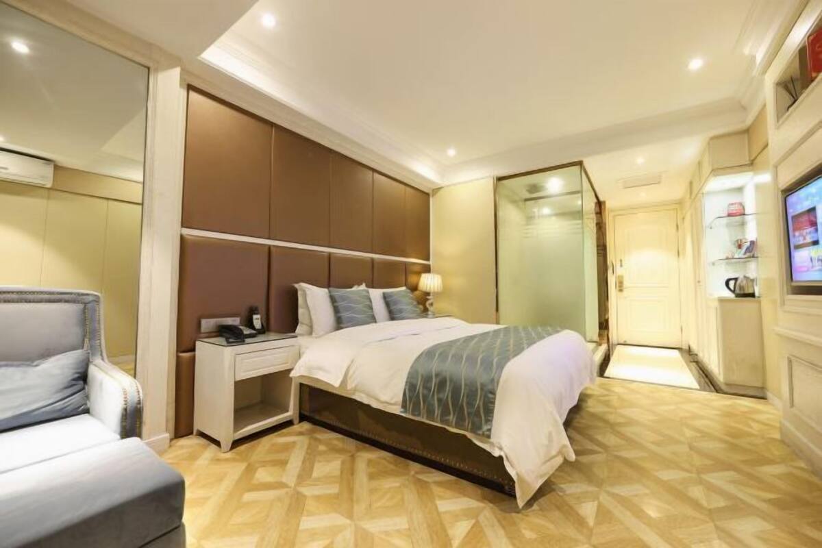 Quarto de hotel com cama, mesa de cabeceira, cadeira e televisão.