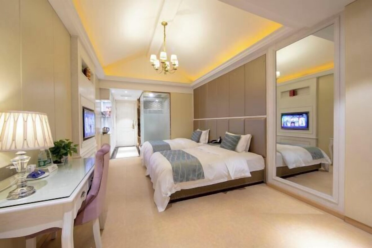 A hotel room with a bed, a desk, a chair, a television, and a mirror.