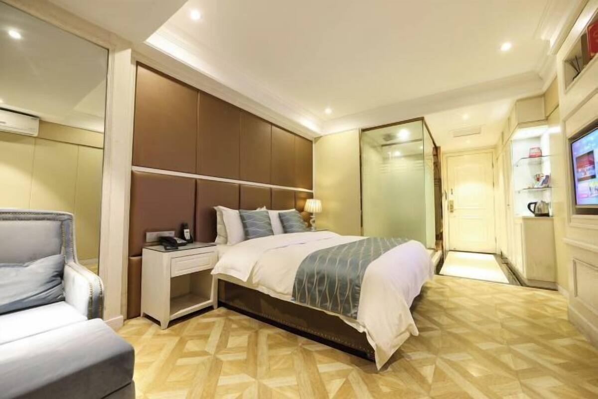 Um quarto com cama, mesa de cabeceira, abajur e televisão.