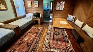 Una habitación acogedora con una cama, una mesita, un televisor y un sofá. Hay alfombras en el suelo y cuadros en las paredes.