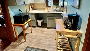 Cocina compacta con armarios grises, un microondas sobre una mesita, cafetera y lavabo.
