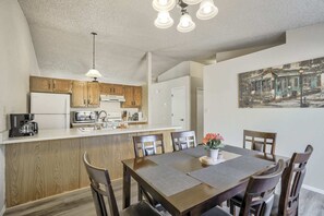 A modern kitchen with wooden cabinets, a white refrigerator, and a dining area with a table and chairs.