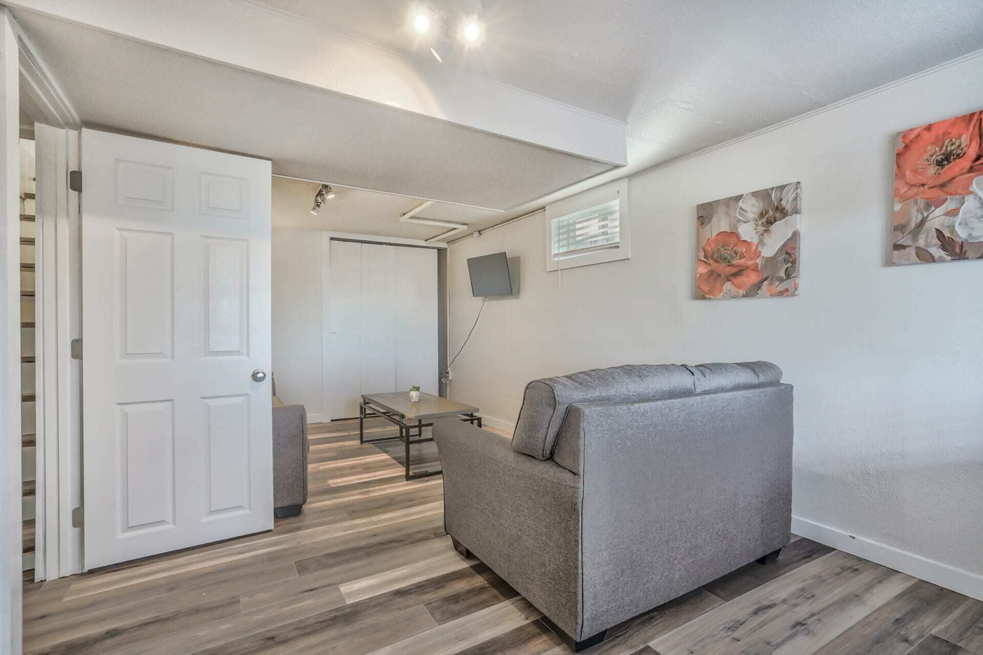 A compact living space with a grey sofa, a small table, and a TV mounted on the wall.