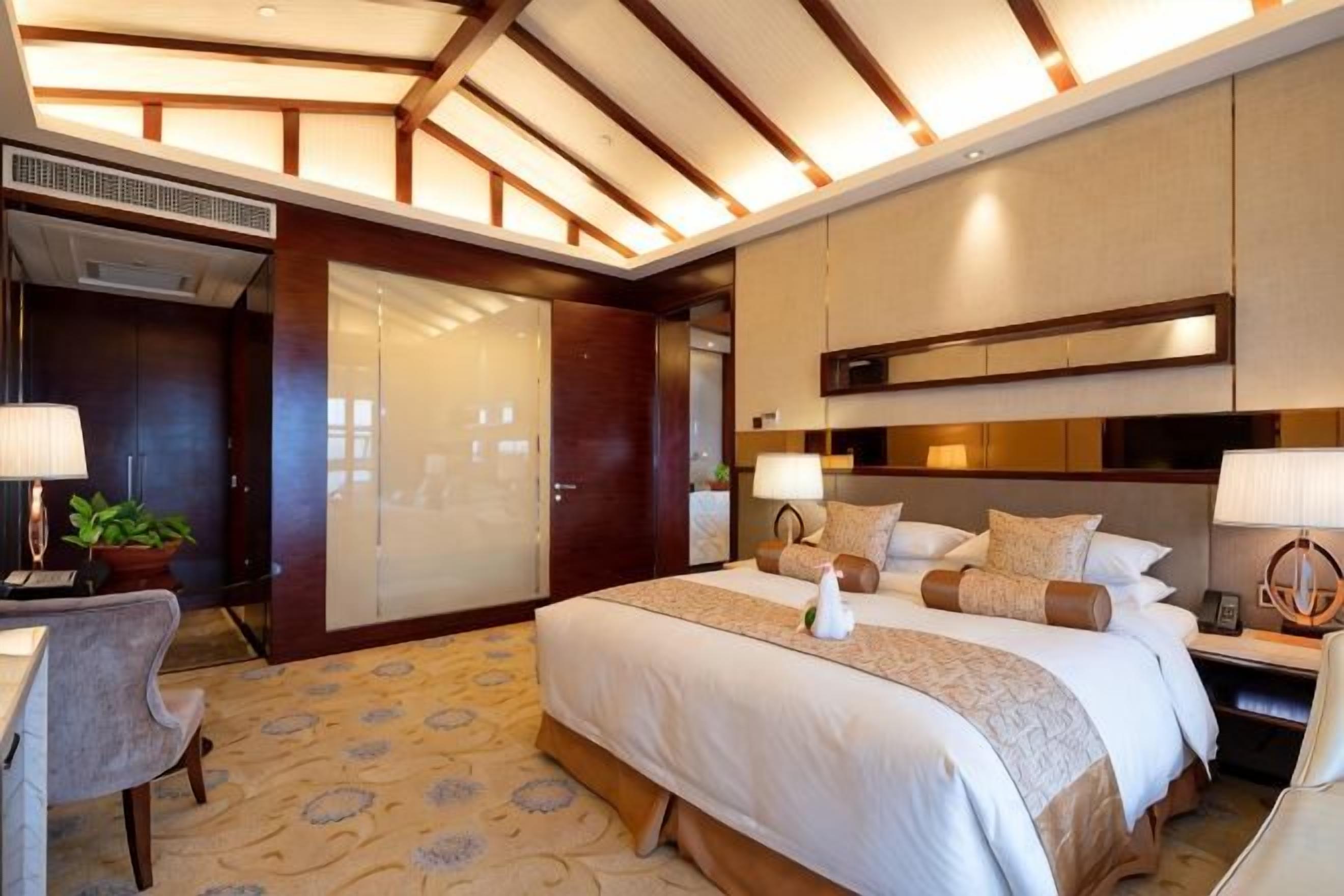 A hotel room with a large bed, bedside tables, a desk, and a wardrobe.