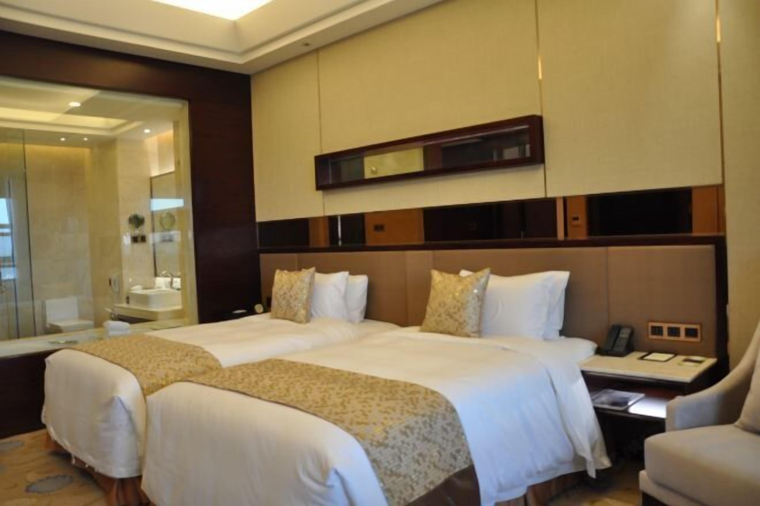 Habitación de hotel con dos camas, un espejo grande, una mesita de noche con teléfono y una silla.