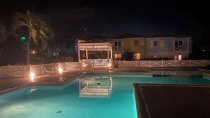 A nighttime view of a swimming pool area with a covered seating area and a building in the background. - Southgate courtyard<br>Unit 20 (Christiansted)