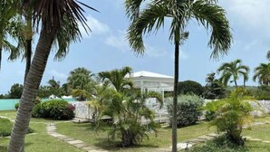 A well-maintained garden with palm trees, a white gazebo, and a stone pathway leading to a white building. - Southgate courtyard<br>Unit 20 (Christiansted)