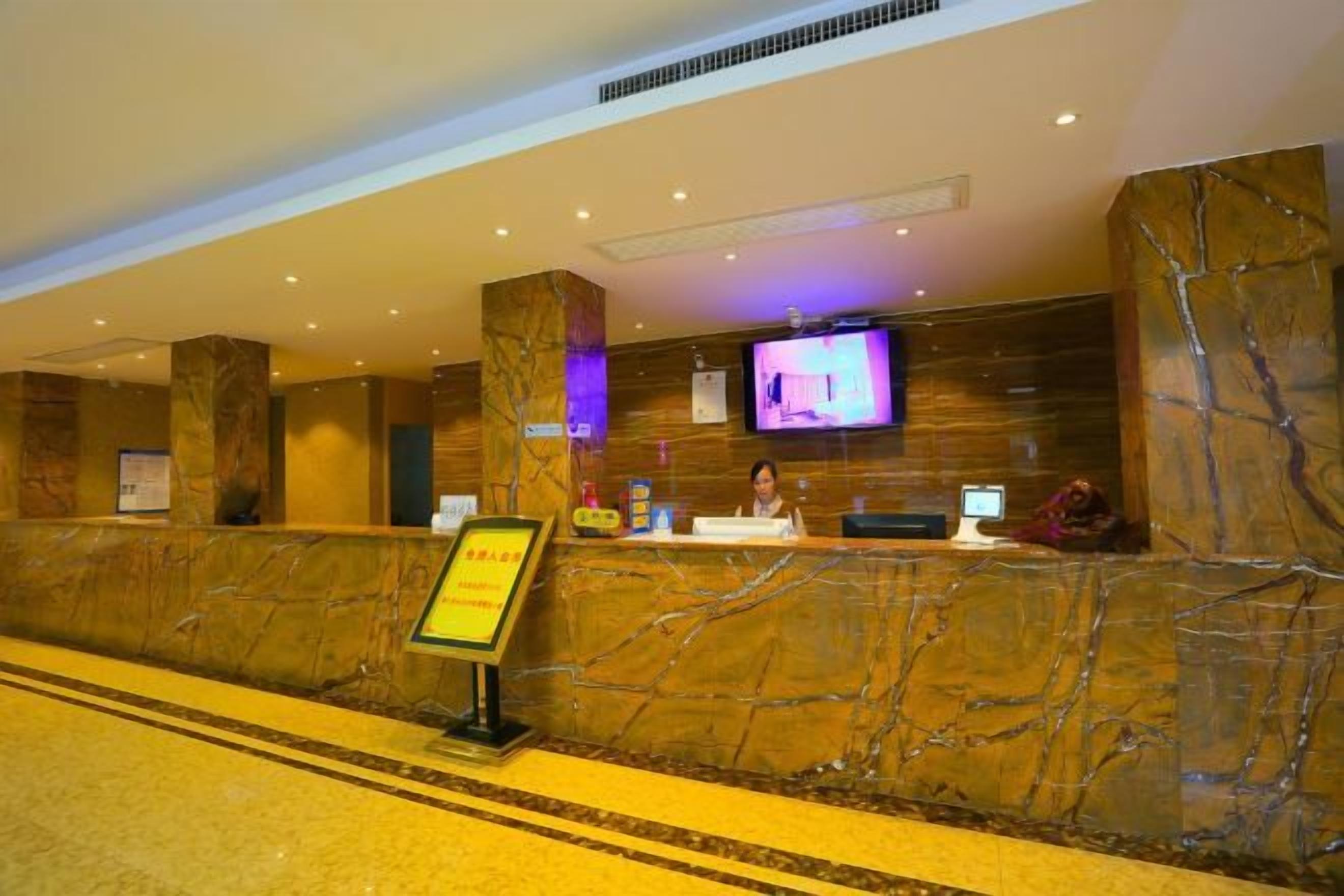 A hotel reception area with marble walls, a reception desk, a television screen, and a signboard.