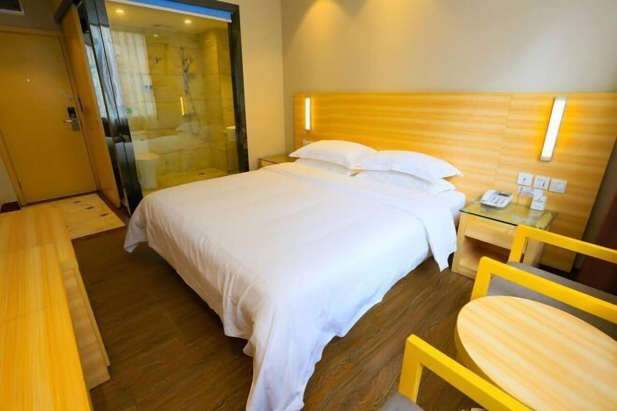 A hotel room with a bed, bedside table, chair, and a glass-enclosed shower area.
