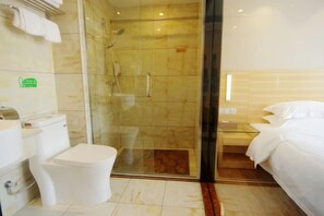 Un baño de hotel con ducha de vidrio, inodoro y cama.
