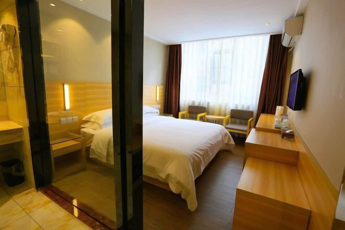 A hotel room with a bed, a desk, a chair, a TV, and a window with curtains.