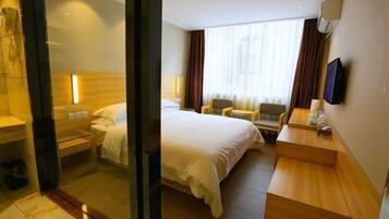 Habitación de hotel con cama, escritorio, silla, televisor y ventana con cortinas.