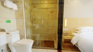 A hotel bathroom with a glass-enclosed shower, a toilet, and a bed with white bedding. - Zhongya Hotel (Nanning)