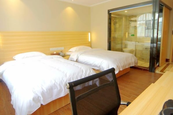 A hotel room with two beds, a wooden headboard, a desk, and a glass shower enclosure. - Zhongya Hotel (Nanning)