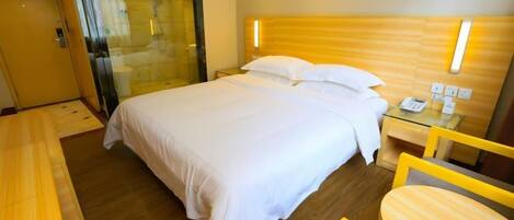 A hotel room with a bed, bedside table, and a glass-enclosed shower area.