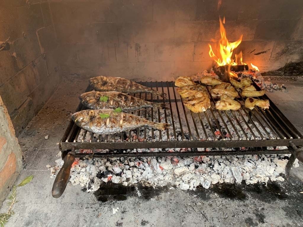 A grill with various meats and vegetables being cooked over an open flame.