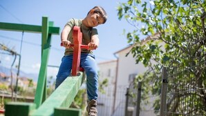 Une personne utilise une balançoire dans un espace extérieur, avec une structure verte et une clôture métallique en arrière-plan.