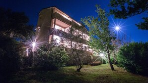 A multi-story building with a flat roof and balconies, surrounded by trees and illuminated by multiple light sources. - Apartment in Lopar with Balcony, Air condition, WIFI (4739-4) (Lopar)