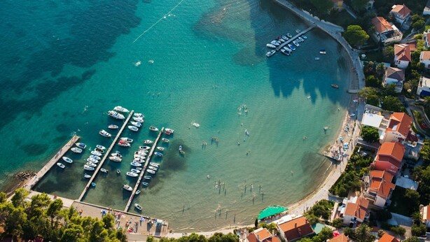 An aerial view of a coastal marina with boats docked, a sandy beach, and residential buildings with red roofs. - Apartment in Lopar with Balcony, Air condition, WIFI (4739-4) (Lopar)