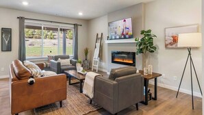 A modern living room with a fireplace, a television, and a large window overlooking a garden.