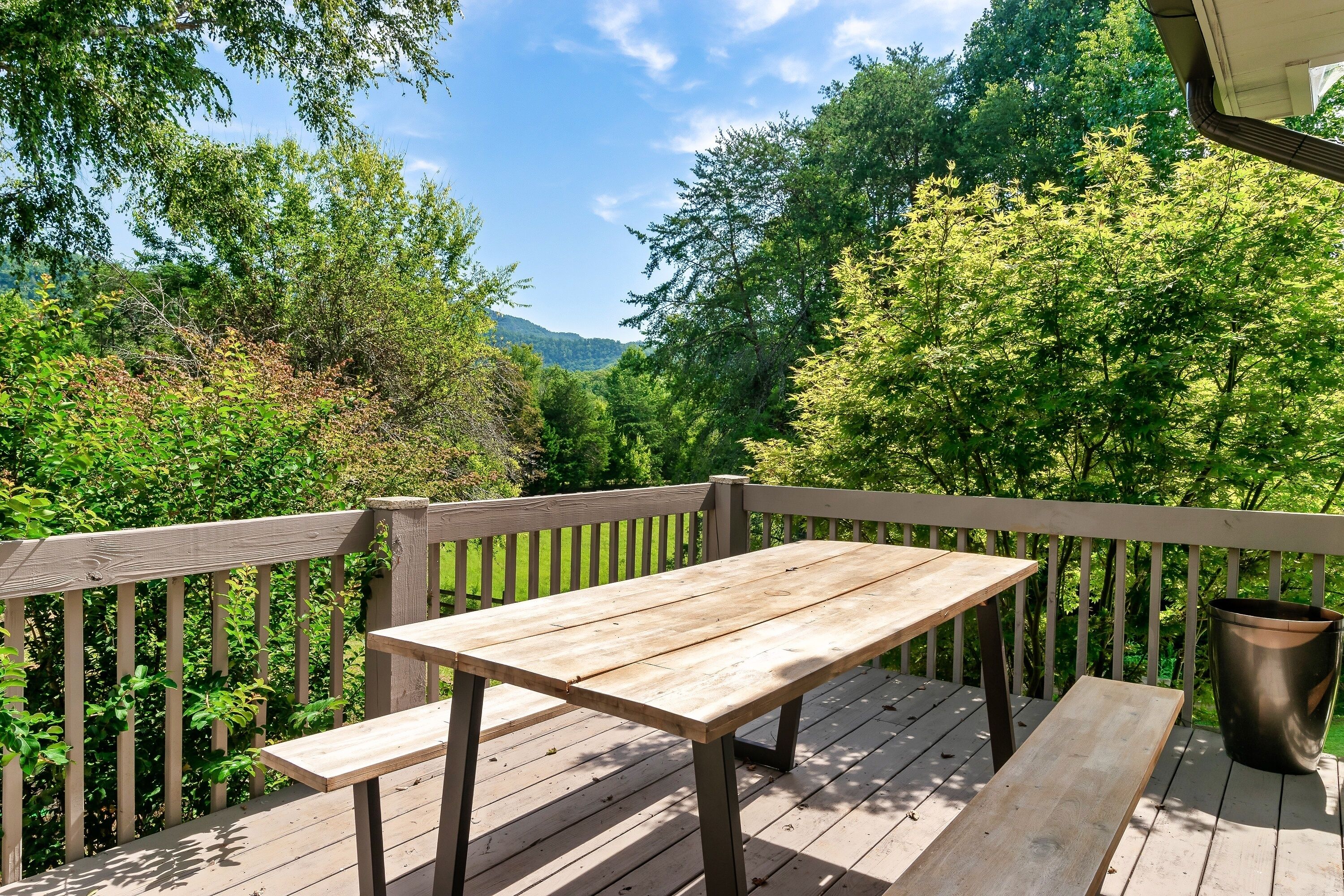 Eine Holzterrasse mit Tisch und Bänken, umgeben von üppigem Grün und Bäumen.