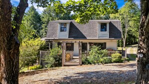 A two-story house with a covered porch, surrounded by trees and a gravel driveway. - True Family Getaway! Awesome Views | Easy Access (Townsend)