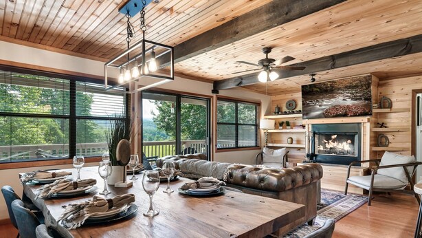 A spacious dining area with a long wooden table set for a meal, a leather sofa, and a fireplace. - True Family Getaway! Awesome Views | Easy Access (Townsend)
