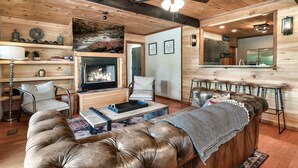 A cozy living room with a fireplace, leather sofa, and a dining area with a high chair. - True Family Getaway! Awesome Views | Easy Access (Townsend)