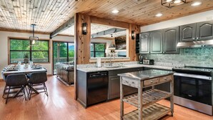 A modern kitchen with wooden ceiling beams, large windows, and a central island with a dishwasher and oven. - True Family Getaway! Awesome Views | Easy Access (Townsend)