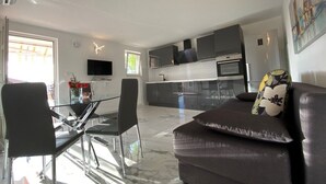 A modern kitchen with a flat-screen TV, a dining area with a glass table and chairs, and a living area with a sofa and a painting. - Apartment in Okrug Gornji with Balcony, Air condition, WIFI, Dishwasher (5048-1) (Okrug Gornji)